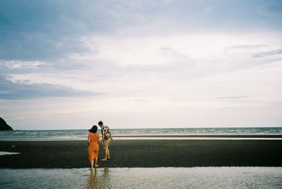 Rear view of friends standing on beach against sky