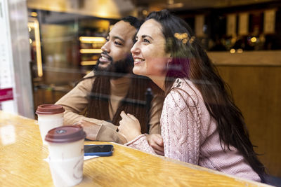 Smiling man and woman with coffee cups sitting at table in cafe