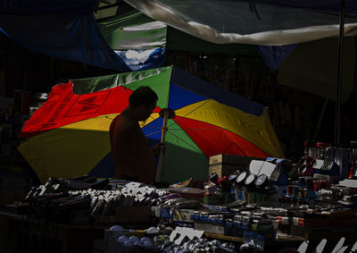 Vendor holding colorful parasol by market stall