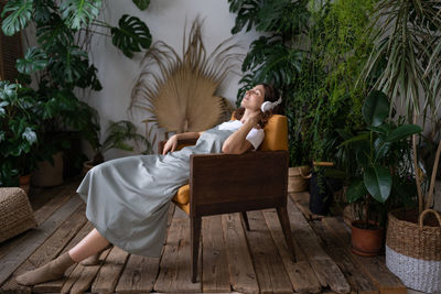 Relaxed woman in earphones rest after work in indoor greenhouse. stress relief and wellbeing concept