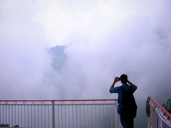 Rear view of man photographing against sky