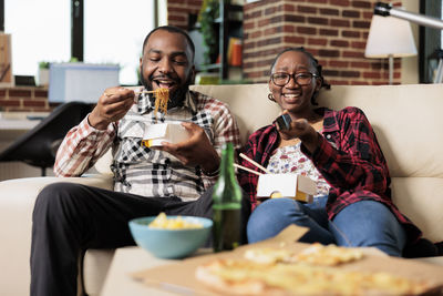 Happy woman watching tv by man eating noodles