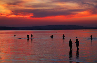 Silhouette people at beach against sky during sunset