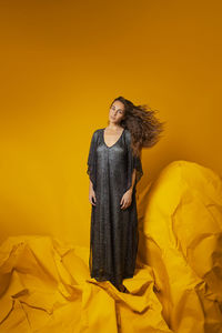 Young woman standing against yellow background