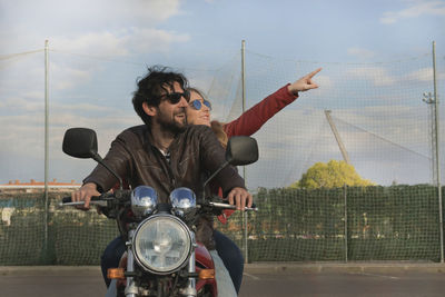 Couple riding motorcycle on road against sky