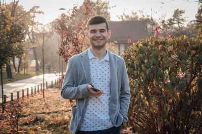 Portrait of smiling young man standing by plants during autumn