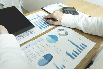 Midsection of man with digital tablet analyzing chart on table