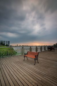 Empty bench in city against sky during sunset