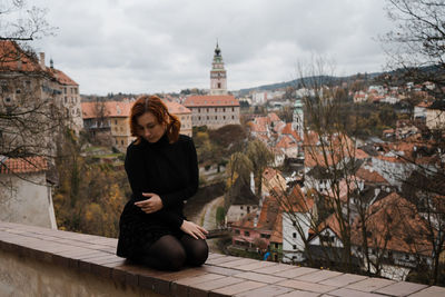 Full length of woman kneeling on retaining wall in city