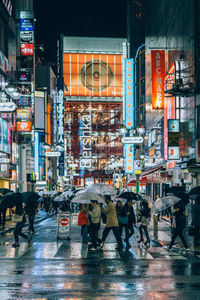 People holding umbrella while walking on street amidst illuminated buildings at night