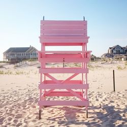 Pink lifeguard chair on sand at beach against clear sky