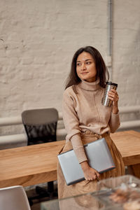 Young woman holding coffee cup looking away at cafe