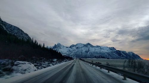 Snow covered road by mountain against sky