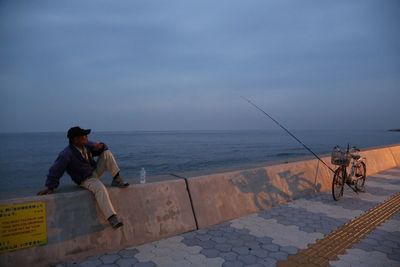 Men fishing at sea shore against sky