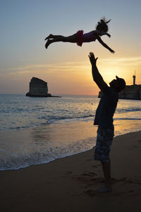 Silhouette people on beach against sky during sunset