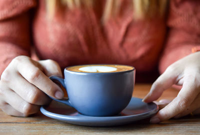 Midsection of woman holding coffee cup on table