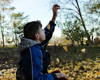 A boy sitting under a tree in the garden catches falling autumn leaves