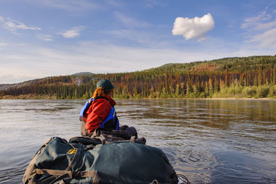 Side view of hiker canoeing on river against cloudy sky at forest