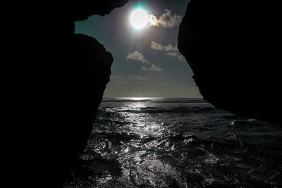 Silhouette rock formations on sea against sky