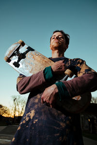 Low angle view of man with skateboard standing against sky