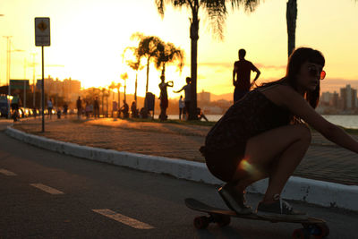 Young woman skateboarding on street during sunset