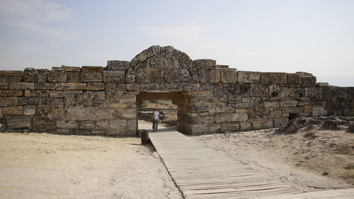 Rear view of woman walking on boardwalk through old ruined entrance