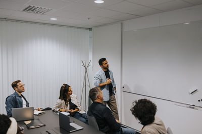 Mature businessman explaining strategy on whiteboard to colleagues in board room at office