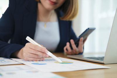 Midsection of woman using smart phone on table