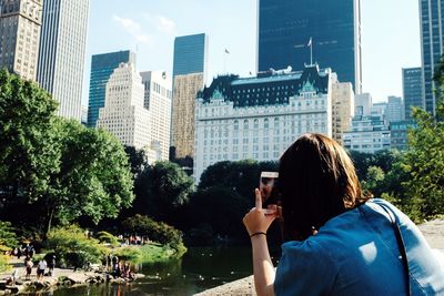 Woman photographing buildings while using smart phone at central park