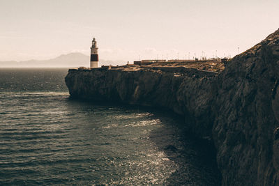 Lighthouse on cliff over sea against sky