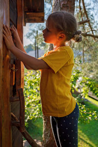 Girl plays in creative handmade treehouse in backyard, summer activity, happy childhood, cottagecore