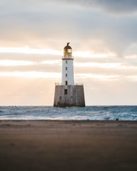 Lighthouse on beach by sea against sky