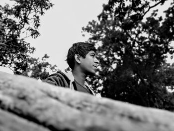 Low angle view of young man looking away against trees