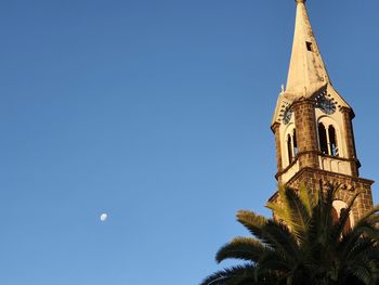 Low angle view of palm tree and building against blue sky