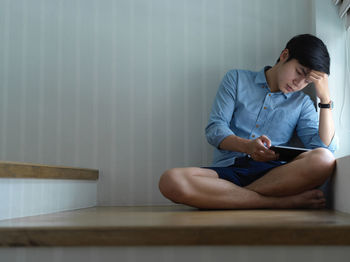 Young man using digital tablet sitting on staircase at home