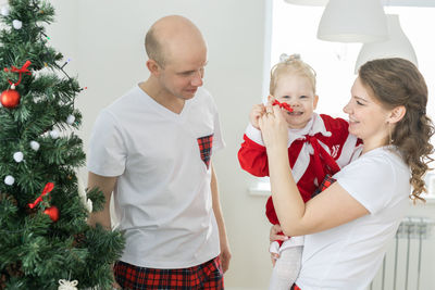 Side view of couple standing against christmas tree at home