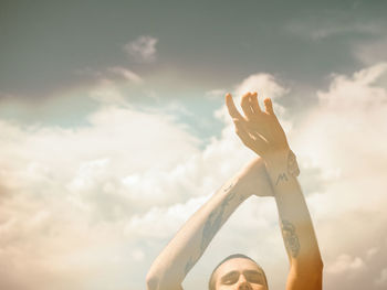 High section of man with arms raised against sky on sunny day