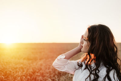 Beautiful woman standing on field against clear sky during sunset