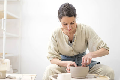Mid adult potter holding bowl while sitting in workshop