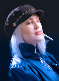 Portrait of young woman wearing hat against black background