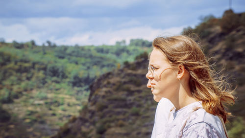 Side view of young woman standing against mountain