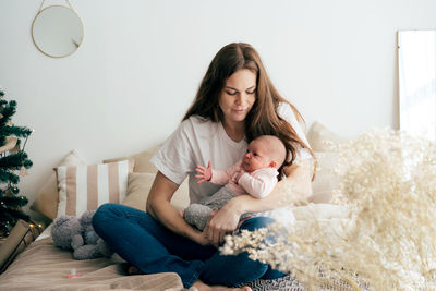 Gentle caring mother holds a newborn baby in her arms while sitting on the bed.