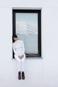 Sad young woman standing on window of white building