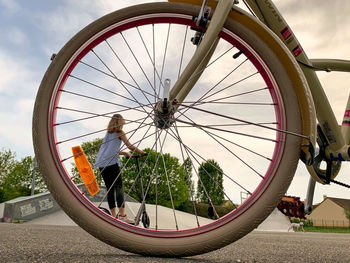 Reflection of woman on bicycle wheel against sky