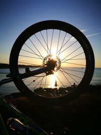 Silhouette wheel by sea against sky during sunset