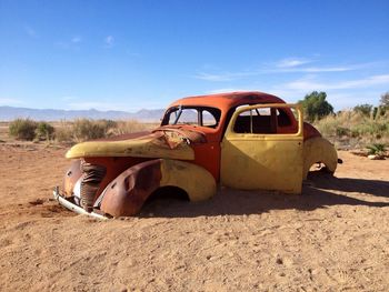 Abandoned vintage car on sand against blue sky