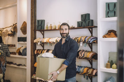 Portrait of smiling male sales clerk carrying box at fashion boutique door handle