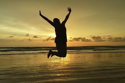 Silhouette woman jumping on beach against sky during sunset