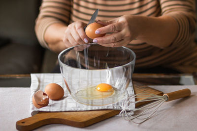 Old woman's hands cracking eggs into glass bowl with knife. prepare for making breakfast.