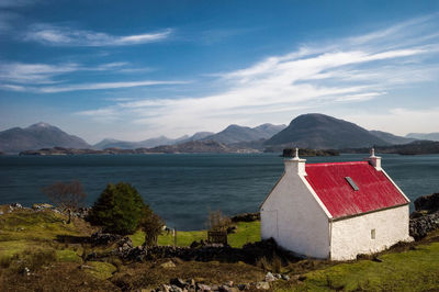 House at lakeshore by mountains against sky